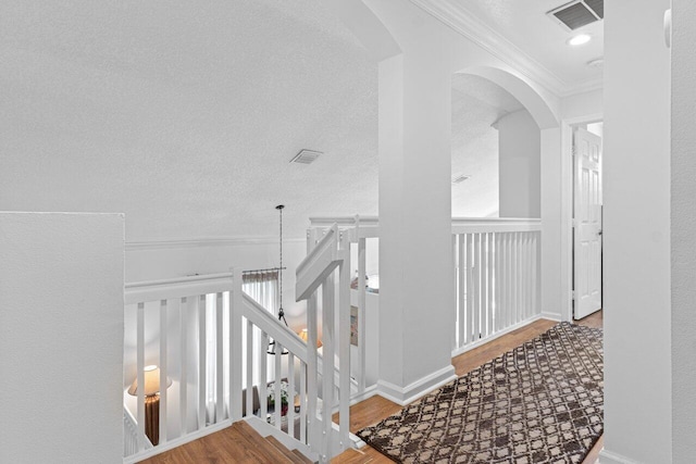 hallway featuring ornamental molding, wood-type flooring, and a textured ceiling