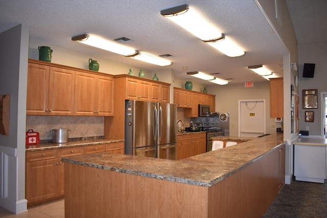 kitchen with kitchen peninsula, light tile floors, backsplash, stainless steel refrigerator, and a textured ceiling