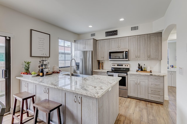 kitchen with stainless steel appliances, a kitchen breakfast bar, light hardwood / wood-style flooring, sink, and light stone counters