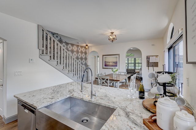 kitchen with a notable chandelier, light hardwood / wood-style floors, sink, light stone counters, and dishwasher