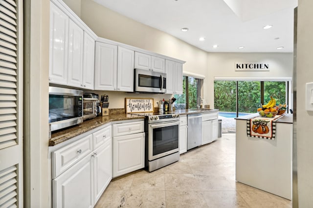 kitchen featuring white cabinetry, appliances with stainless steel finishes, sink, dark stone countertops, and light tile floors