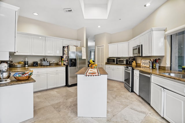 kitchen featuring a kitchen island, stainless steel appliances, white cabinets, and light tile floors