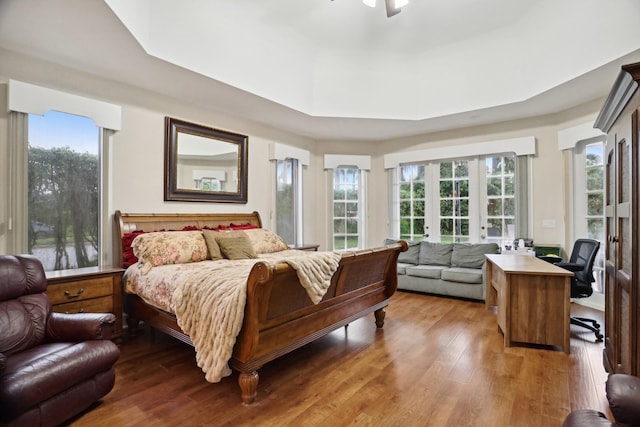 bedroom featuring french doors, light hardwood / wood-style floors, ceiling fan, and a tray ceiling