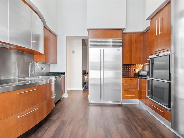 kitchen with dark stone counters, backsplash, stainless steel appliances, dark wood-type flooring, and a high ceiling