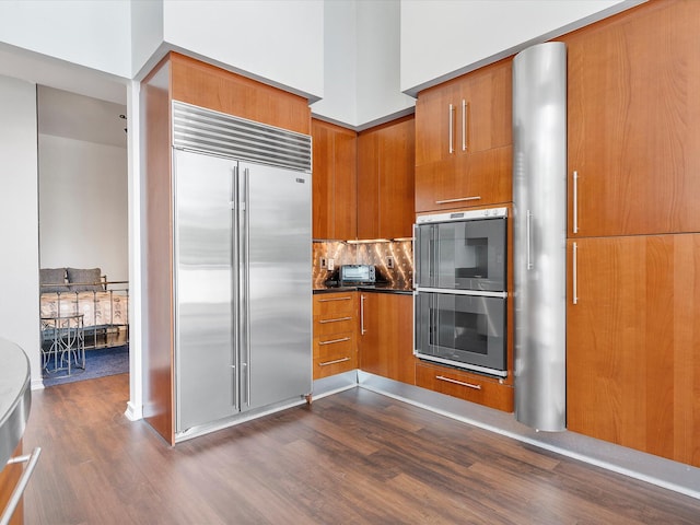 kitchen featuring a high ceiling, backsplash, dark hardwood / wood-style floors, double oven, and built in refrigerator