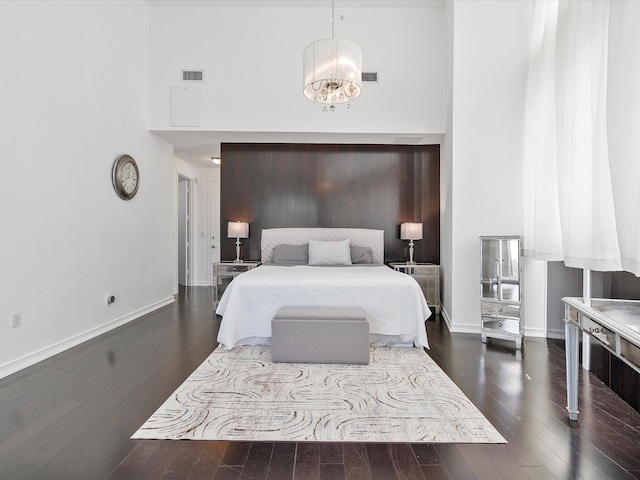 bedroom with dark hardwood / wood-style floors, an inviting chandelier, and a high ceiling