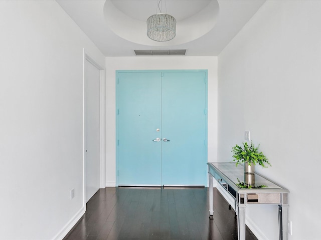 hall featuring an inviting chandelier, a raised ceiling, and dark hardwood / wood-style flooring