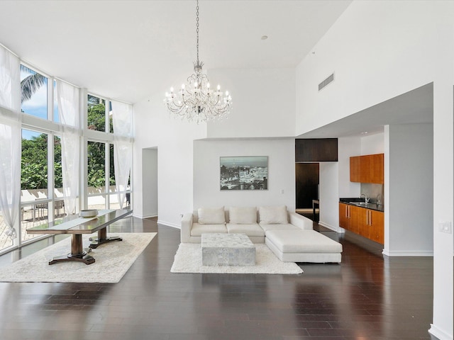 living room with a notable chandelier, dark wood-type flooring, a towering ceiling, and sink