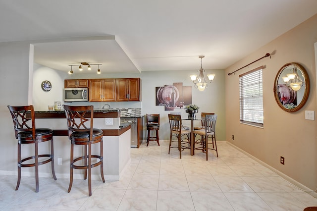 kitchen featuring a breakfast bar, track lighting, appliances with stainless steel finishes, light tile floors, and a chandelier