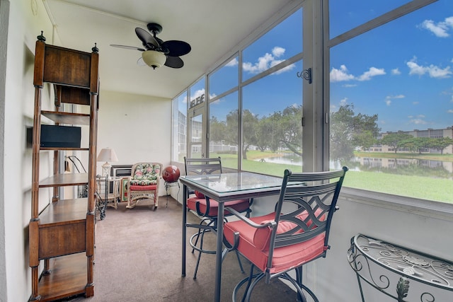 sunroom with ceiling fan and a water view