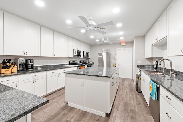 kitchen featuring ceiling fan, light hardwood / wood-style floors, sink, dark stone countertops, and a center island