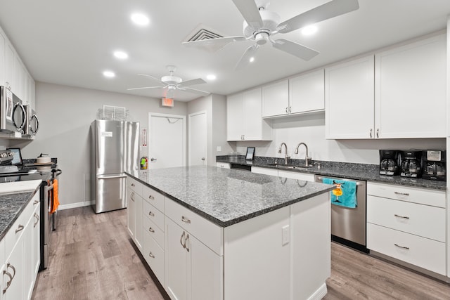 kitchen with ceiling fan, dark stone counters, a kitchen island, stainless steel appliances, and light wood-type flooring