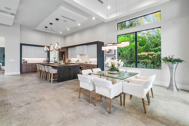 tiled dining space featuring a raised ceiling, an inviting chandelier, sink, and a high ceiling