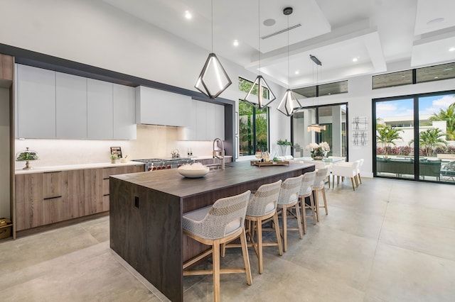 kitchen featuring an island with sink, hanging light fixtures, a kitchen breakfast bar, and white cabinetry