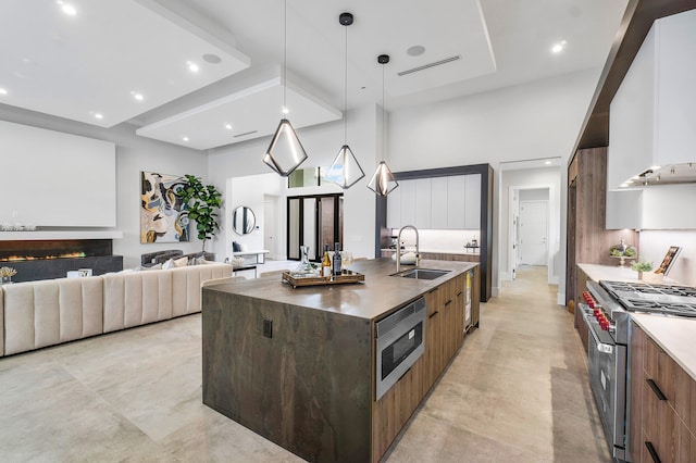 kitchen with hanging light fixtures, appliances with stainless steel finishes, sink, light tile floors, and a center island with sink