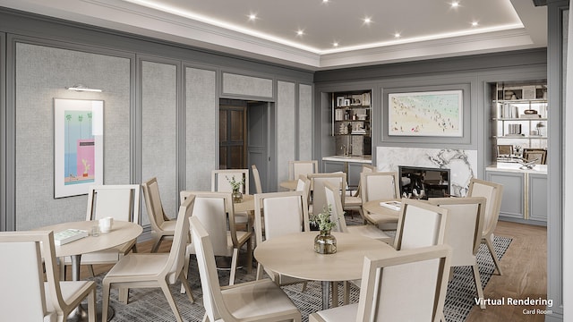 dining area with ornamental molding, a raised ceiling, a high end fireplace, and hardwood / wood-style floors