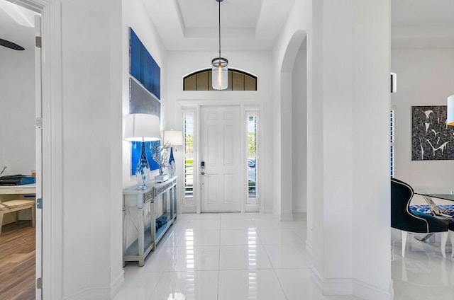 foyer with a towering ceiling, a tray ceiling, and light wood-type flooring