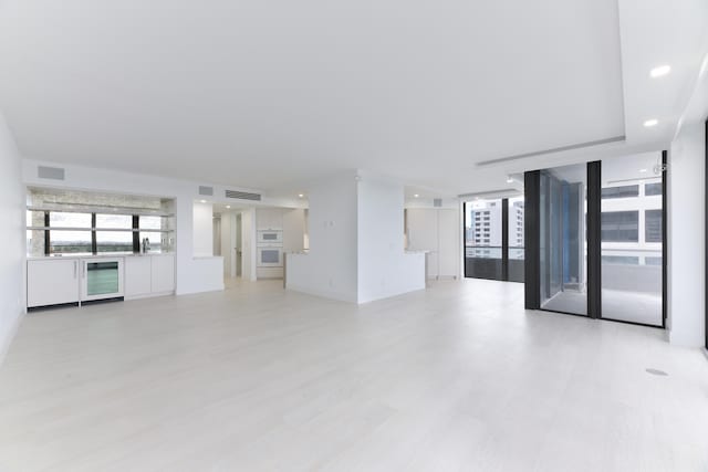 unfurnished living room with wine cooler, light hardwood / wood-style flooring, and a wall of windows