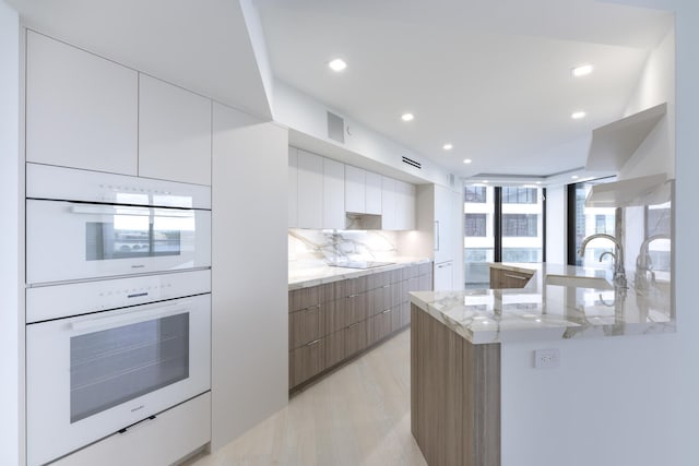 kitchen featuring tasteful backsplash, double oven, white cabinetry, and light stone countertops