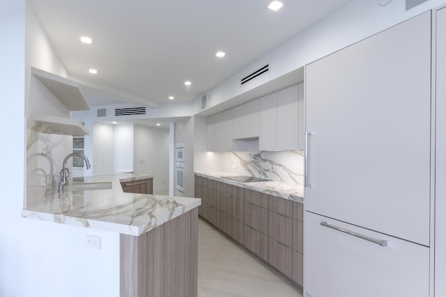 kitchen featuring white cabinetry, sink, backsplash, kitchen peninsula, and light stone countertops