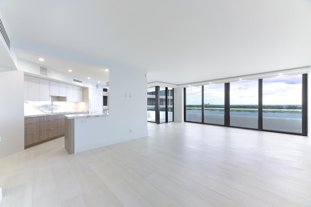 unfurnished living room with floor to ceiling windows, a water view, and light hardwood / wood-style floors