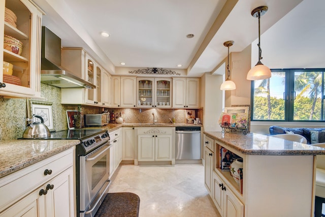 kitchen featuring tasteful backsplash, stainless steel appliances, wall chimney range hood, light stone countertops, and hanging light fixtures