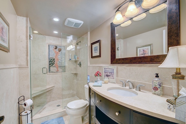 bathroom with a shower with door, vanity, toilet, and tile walls