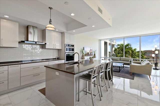 kitchen featuring wall chimney range hood, sink, decorative backsplash, decorative light fixtures, and cooktop