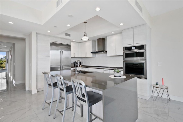 kitchen featuring sink, wall chimney range hood, tasteful backsplash, decorative light fixtures, and a center island with sink