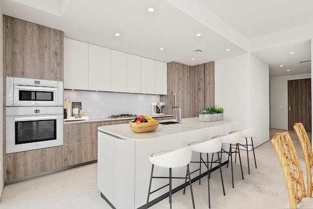 kitchen with kitchen peninsula, double oven, a breakfast bar, sink, and white cabinets