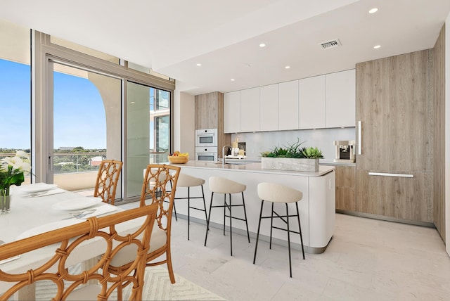 kitchen with light tile floors, a kitchen bar, white cabinetry, a kitchen island with sink, and sink