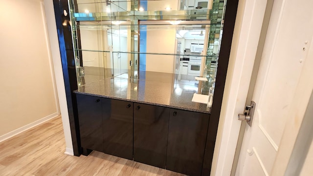 interior space with light wood-type flooring, dark brown cabinetry, white oven, and dark stone countertops