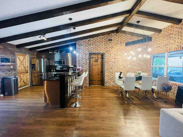 kitchen with brick wall, appliances with stainless steel finishes, vaulted ceiling with beams, and dark hardwood / wood-style floors