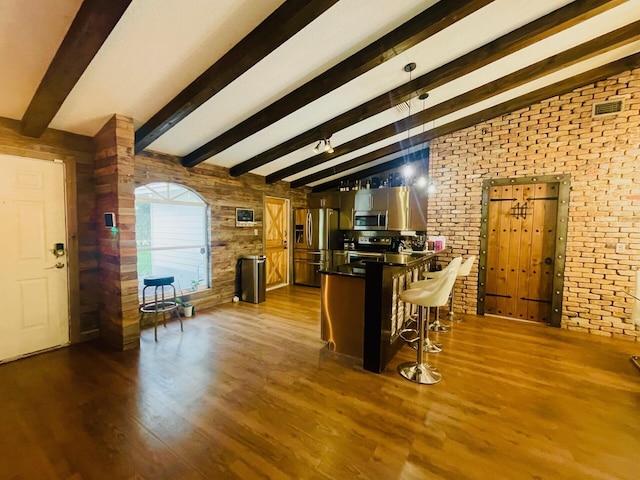 kitchen with dark hardwood / wood-style floors, a kitchen bar, appliances with stainless steel finishes, wood walls, and lofted ceiling with beams