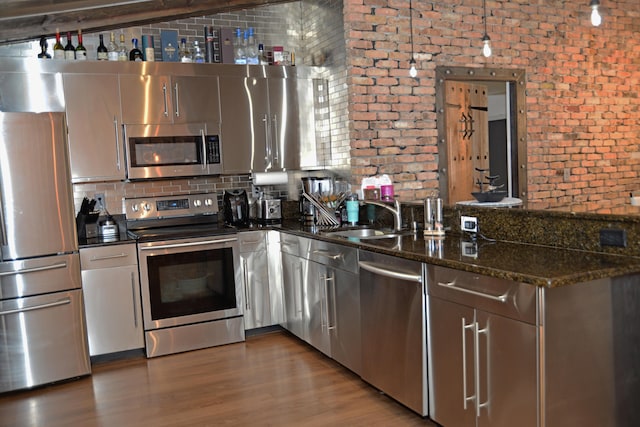 kitchen with backsplash, dark wood-type flooring, brick wall, stainless steel appliances, and dark stone countertops