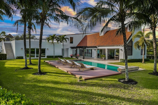 pool at dusk featuring a lawn and a patio area