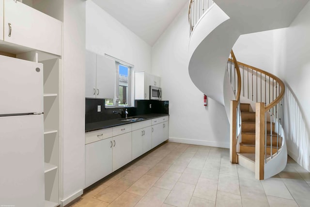 kitchen featuring sink, white fridge, decorative backsplash, light tile patterned floors, and white cabinets