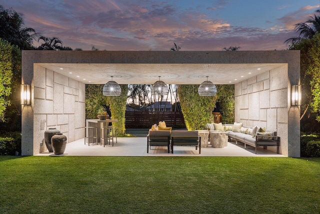 back house at dusk with a lawn, a patio area, and an outdoor living space with a fireplace