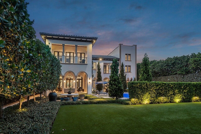 back house at dusk featuring a lawn, a balcony, and french doors