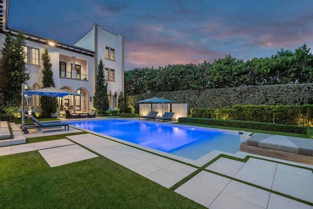 pool at dusk featuring a lawn and a patio