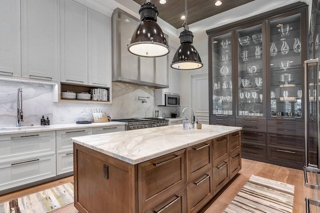 kitchen featuring light hardwood / wood-style floors, tasteful backsplash, white cabinetry, a kitchen island with sink, and light stone counters