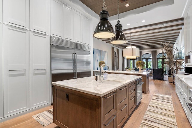 kitchen featuring white cabinets, light stone counters, and a kitchen island with sink