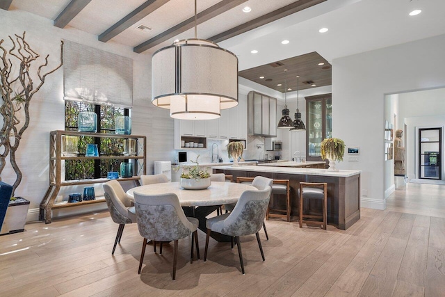 dining room with light hardwood / wood-style flooring, sink, and beamed ceiling