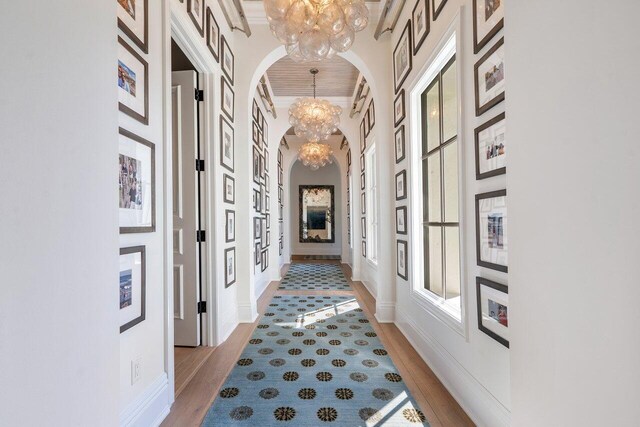 hall featuring a towering ceiling, ornamental molding, a chandelier, and light wood-type flooring