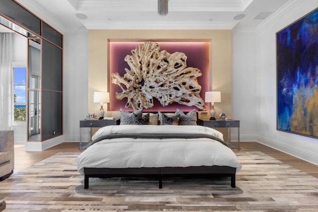 bedroom with crown molding, a raised ceiling, and light wood-type flooring