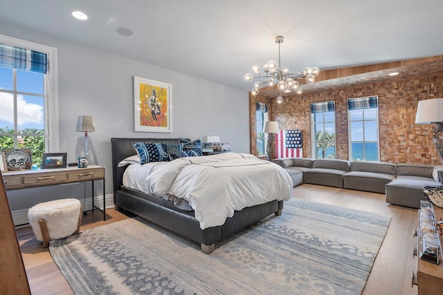 bedroom with brick wall, light hardwood / wood-style floors, multiple windows, and an inviting chandelier