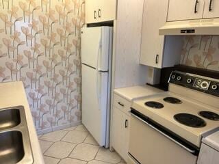 kitchen with white appliances, white cabinets, light tile floors, and premium range hood