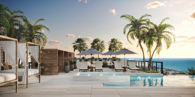 pool at dusk featuring a water view and a patio