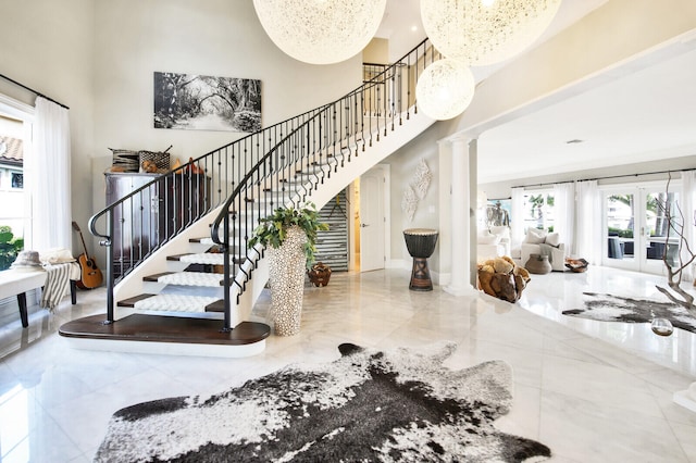 stairs featuring decorative columns, a notable chandelier, light tile floors, a towering ceiling, and french doors