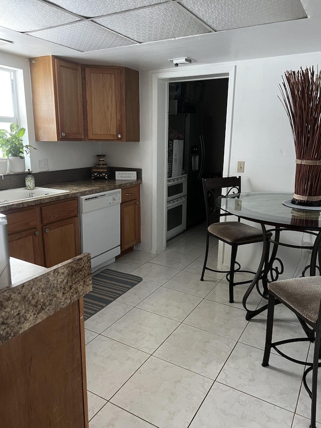 kitchen with white dishwasher, light tile flooring, refrigerator with ice dispenser, stainless steel oven, and sink